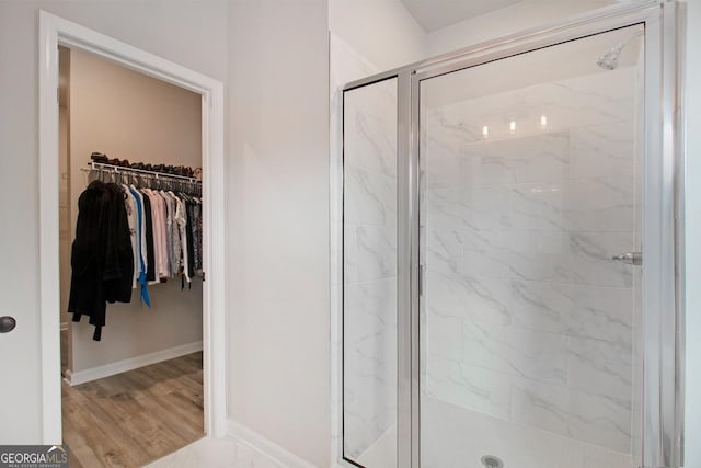 full bathroom with a spacious closet, wood finished floors, a marble finish shower, and baseboards