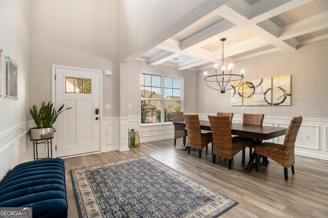 dining space with a decorative wall, coffered ceiling, light wood-style floors, beam ceiling, and an inviting chandelier