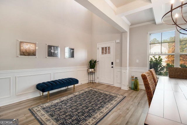 foyer entrance featuring coffered ceiling, wainscoting, light wood-type flooring, a chandelier, and beam ceiling
