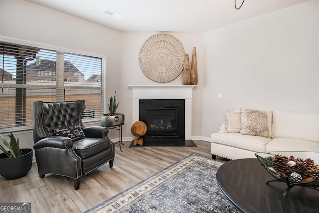 living area with a glass covered fireplace, visible vents, baseboards, and wood finished floors