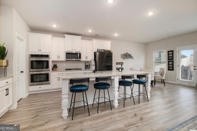 kitchen with recessed lighting, white cabinetry, black appliances, light wood finished floors, and a center island with sink