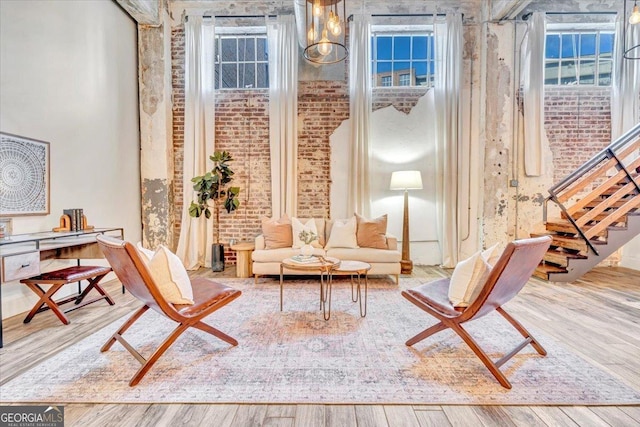 living area with brick wall, a high ceiling, wood finished floors, and stairs