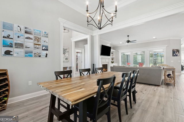 dining space with light wood-type flooring, a warm lit fireplace, and crown molding