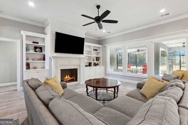 living room with a warm lit fireplace, visible vents, light wood-style floors, and ornamental molding