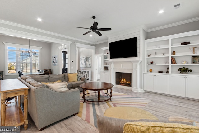 living area with a lit fireplace, light wood-style flooring, crown molding, and ceiling fan with notable chandelier