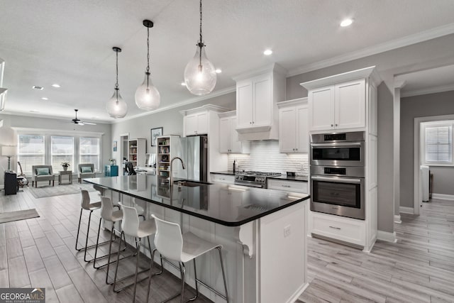 kitchen featuring dark countertops, backsplash, appliances with stainless steel finishes, white cabinets, and a sink