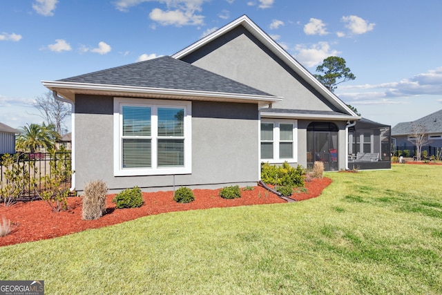 rear view of house with roof with shingles, a lawn, a sunroom, and stucco siding