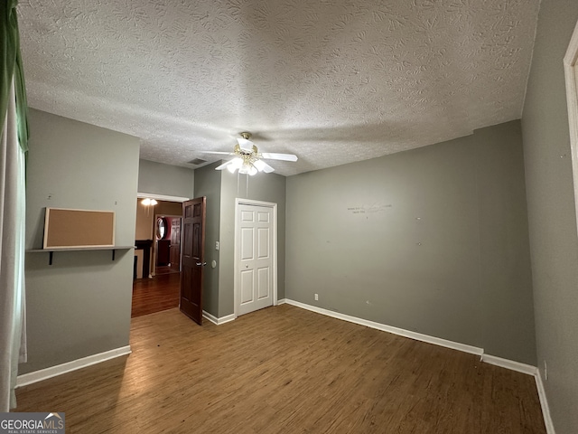 unfurnished bedroom featuring a closet, ceiling fan, a textured ceiling, wood finished floors, and baseboards