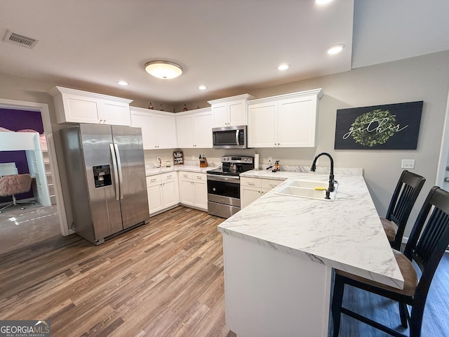 kitchen with stainless steel appliances, visible vents, light wood-style flooring, a sink, and a peninsula