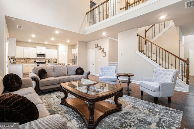 living area featuring dark wood-style flooring, visible vents, a high ceiling, and stairs