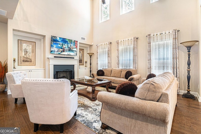 living area with dark wood-style flooring, a fireplace, visible vents, and baseboards