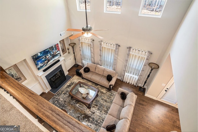 living room featuring a fireplace, visible vents, a towering ceiling, wood finished floors, and baseboards