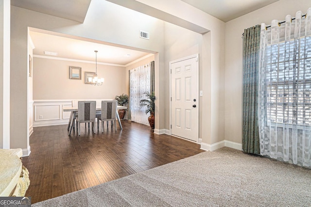 entryway featuring visible vents, dark wood-type flooring, an inviting chandelier, crown molding, and a decorative wall