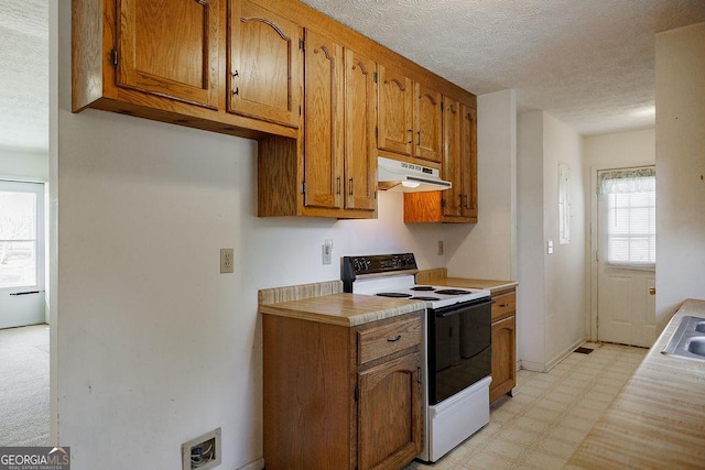 kitchen with brown cabinetry, electric range oven, light floors, light countertops, and under cabinet range hood