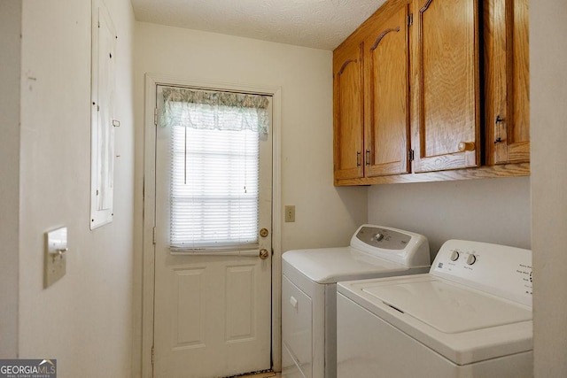 clothes washing area featuring a textured ceiling, washing machine and clothes dryer, and cabinet space