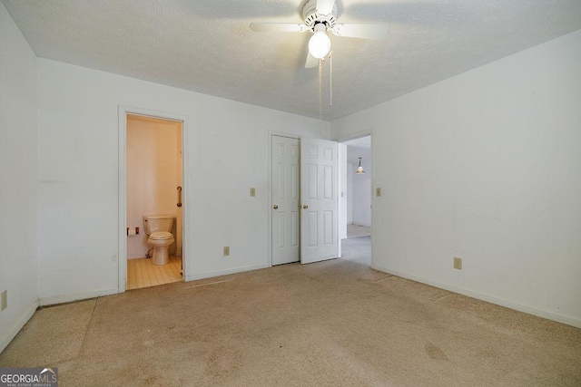 unfurnished bedroom featuring ensuite bath, a textured ceiling, baseboards, and carpet flooring