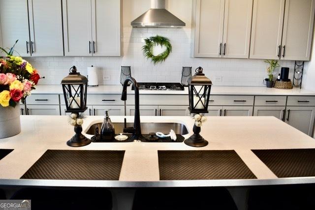 kitchen with gas cooktop, gray cabinetry, light countertops, wall chimney range hood, and tasteful backsplash