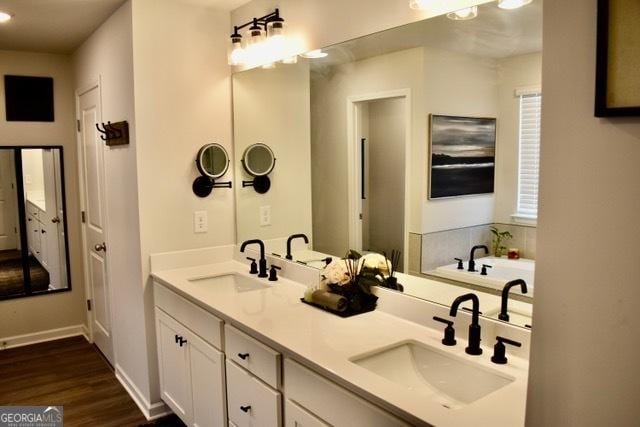 full bath featuring double vanity, wood finished floors, a sink, and a bathing tub