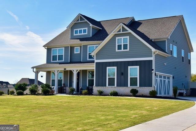 craftsman-style house with a porch, a garage, brick siding, a front lawn, and board and batten siding