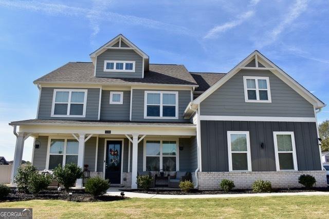 craftsman house featuring board and batten siding, covered porch, brick siding, and a front lawn