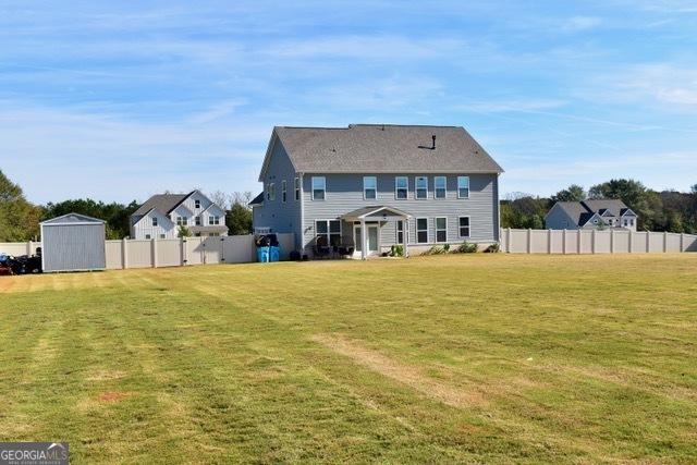 rear view of property with a storage shed, fence, an outbuilding, and a yard