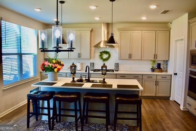 kitchen featuring dark wood finished floors, a kitchen breakfast bar, light countertops, wall chimney range hood, and backsplash