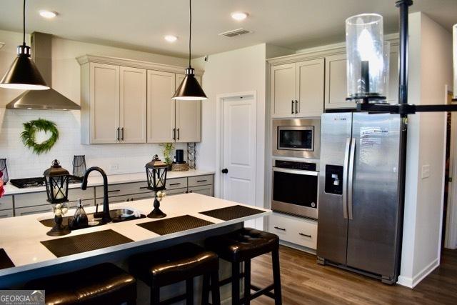 kitchen featuring visible vents, decorative backsplash, appliances with stainless steel finishes, dark wood-type flooring, and wall chimney exhaust hood