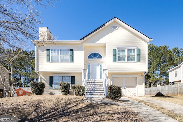 bi-level home with driveway, a garage, a chimney, and fence