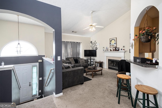 living area with lofted ceiling, ceiling fan, light carpet, a fireplace, and visible vents