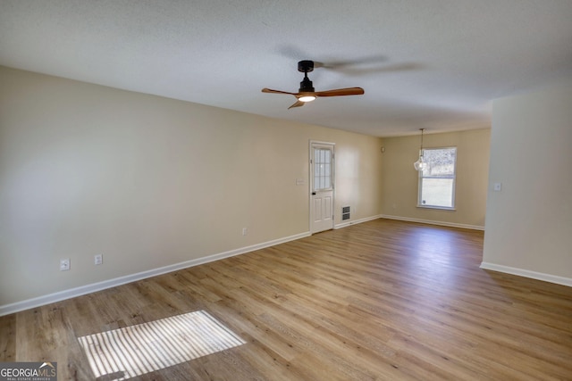 empty room featuring visible vents, light wood-style flooring, ceiling fan, a textured ceiling, and baseboards