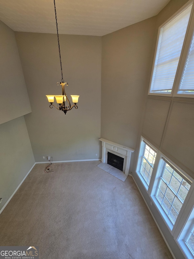 unfurnished living room featuring a chandelier, carpet, a fireplace with flush hearth, and a towering ceiling