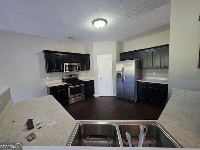 kitchen with dark wood-style floors, stainless steel appliances, light countertops, visible vents, and a sink