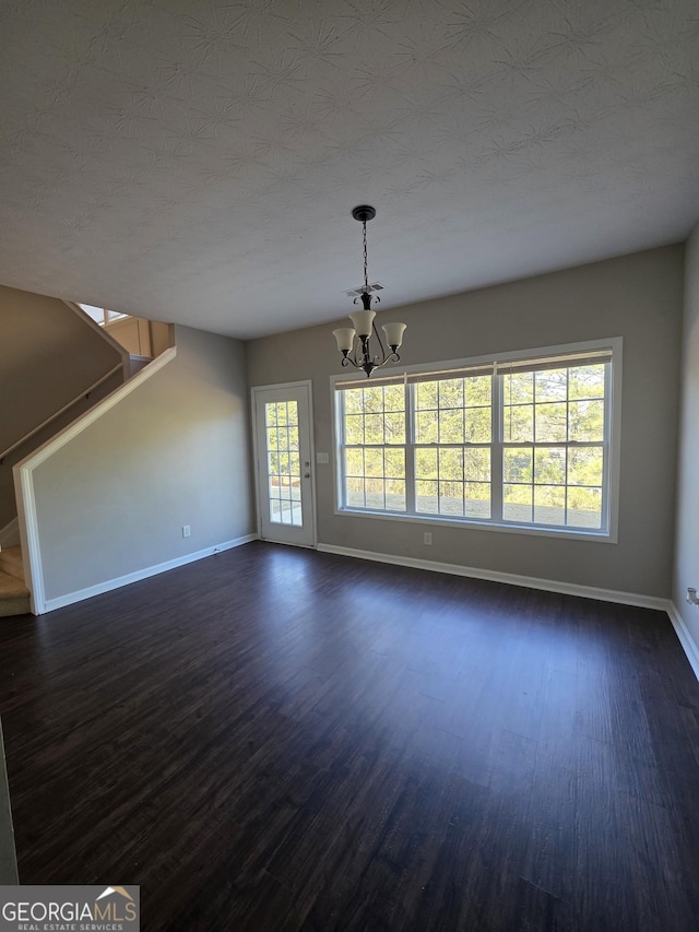 unfurnished living room with baseboards, dark wood-type flooring, stairs, a textured ceiling, and a chandelier