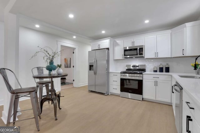 kitchen with light wood finished floors, tasteful backsplash, stainless steel appliances, white cabinetry, and a sink