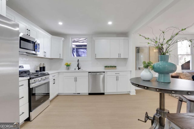 kitchen featuring stainless steel appliances, light countertops, light wood-style floors, white cabinetry, and a sink