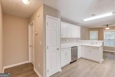 kitchen featuring dishwasher, a peninsula, light countertops, white cabinetry, and a sink