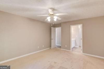 unfurnished bedroom featuring a ceiling fan, ensuite bath, light colored carpet, and baseboards