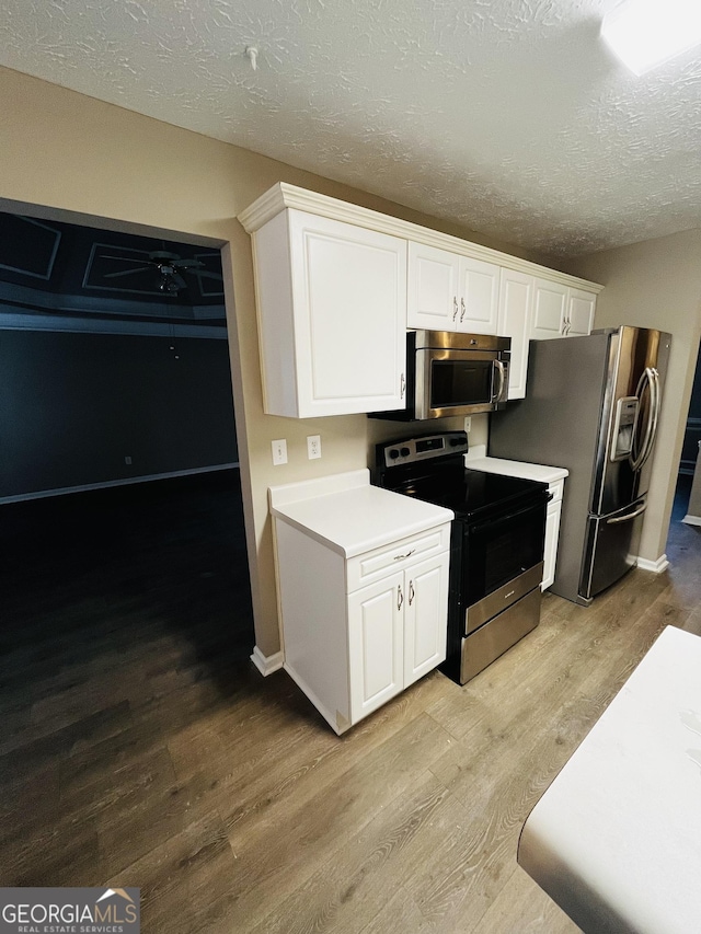 kitchen with appliances with stainless steel finishes, white cabinets, light countertops, and light wood-style floors