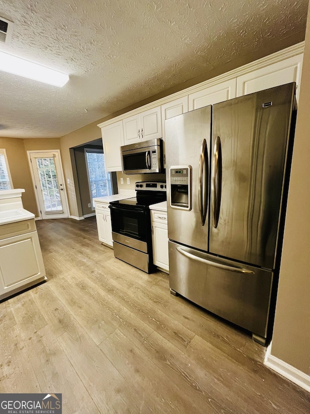 kitchen featuring light wood-style flooring, stainless steel appliances, visible vents, white cabinets, and light countertops