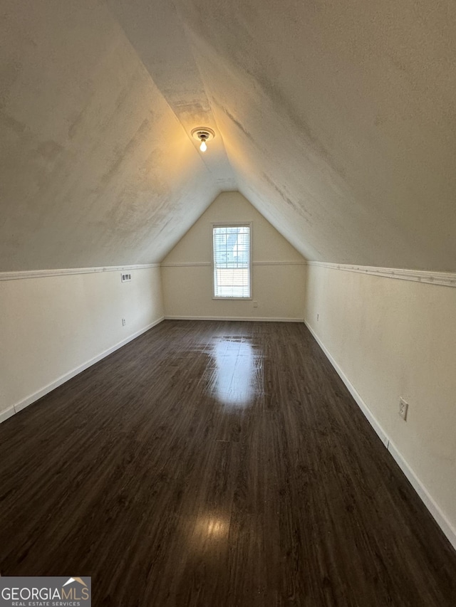 additional living space with dark wood-style floors, baseboards, vaulted ceiling, and a textured ceiling