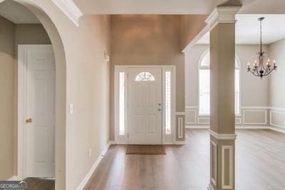 foyer featuring arched walkways, plenty of natural light, wood finished floors, and decorative columns