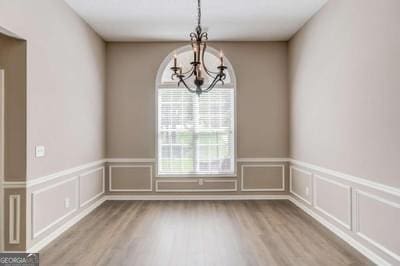 unfurnished dining area with wood finished floors, a decorative wall, and an inviting chandelier