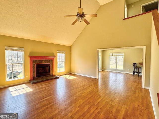 unfurnished living room featuring baseboards, a fireplace with raised hearth, hardwood / wood-style floors, and ceiling fan with notable chandelier