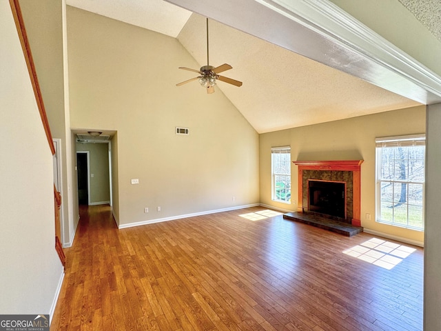 unfurnished living room with visible vents, a tiled fireplace, a ceiling fan, baseboards, and hardwood / wood-style flooring