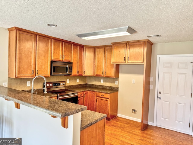 kitchen with stainless steel appliances, brown cabinetry, visible vents, and a peninsula