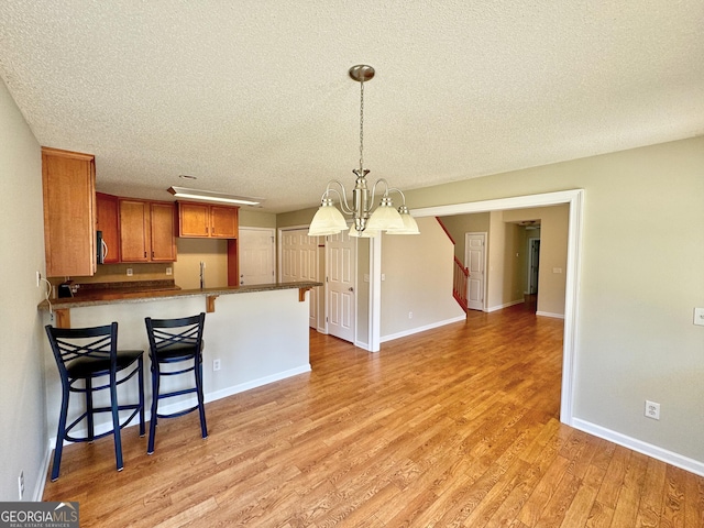 kitchen with brown cabinets, a breakfast bar area, dark countertops, light wood-style floors, and a peninsula