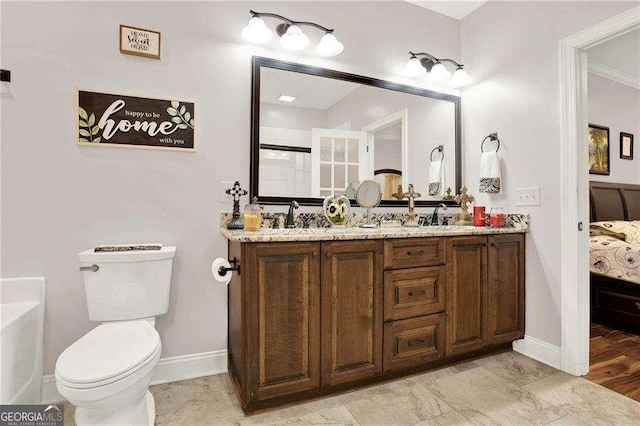 bathroom with double vanity, a sink, toilet, and baseboards