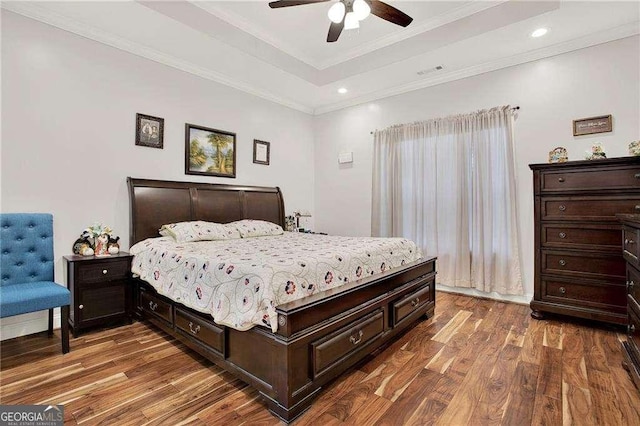 bedroom with ornamental molding, a tray ceiling, visible vents, and wood finished floors