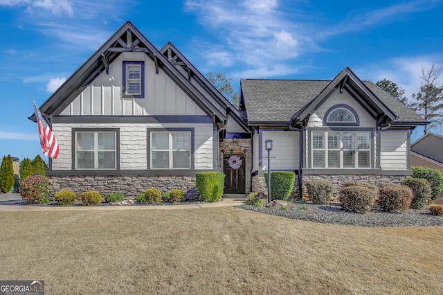 view of front of house featuring stone siding, board and batten siding, a front yard, and roof with shingles