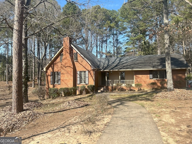 view of front of property with covered porch, brick siding, and a chimney